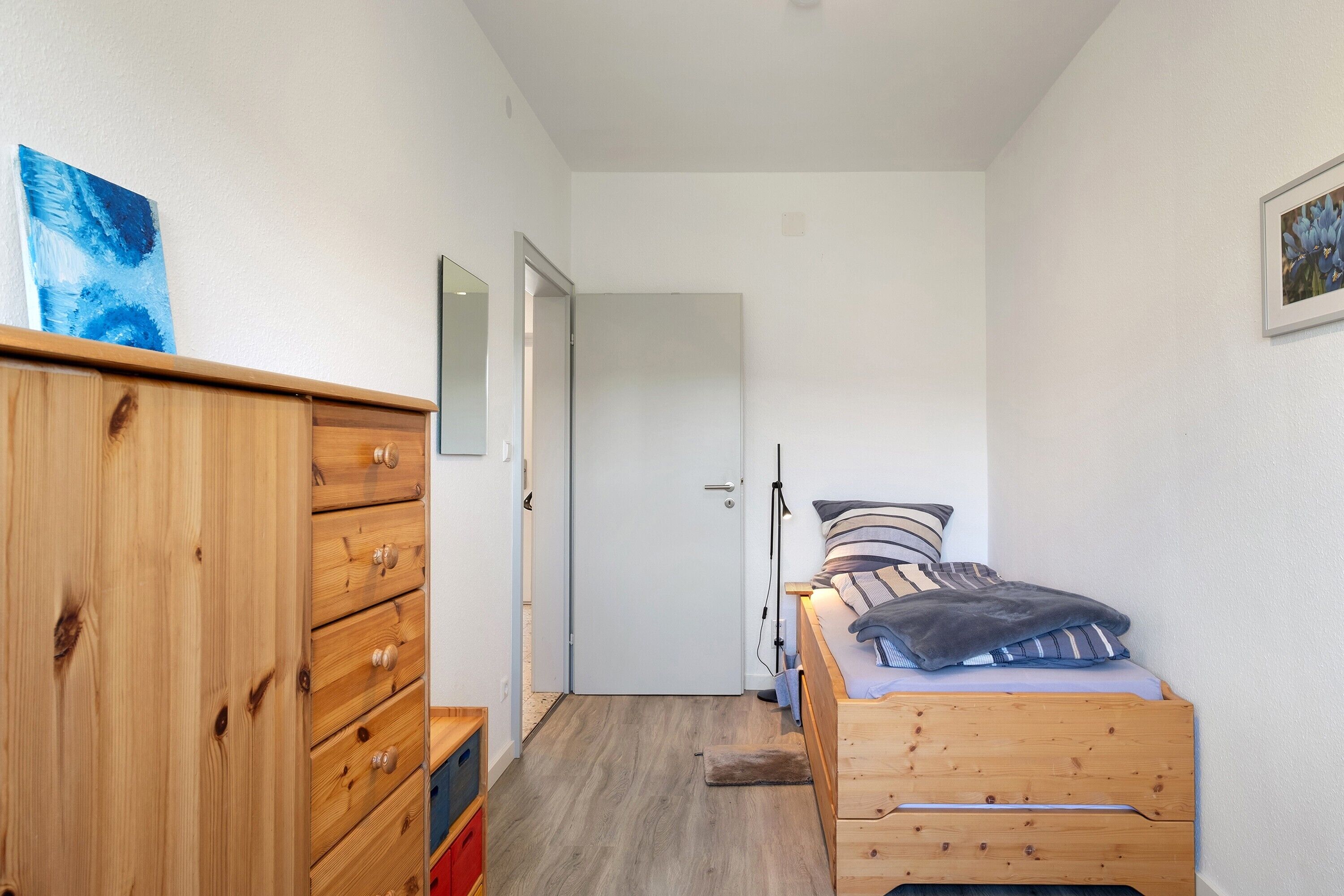 A bedroom with a wooden dresser, a bed with pillows, a door, and a small rug.