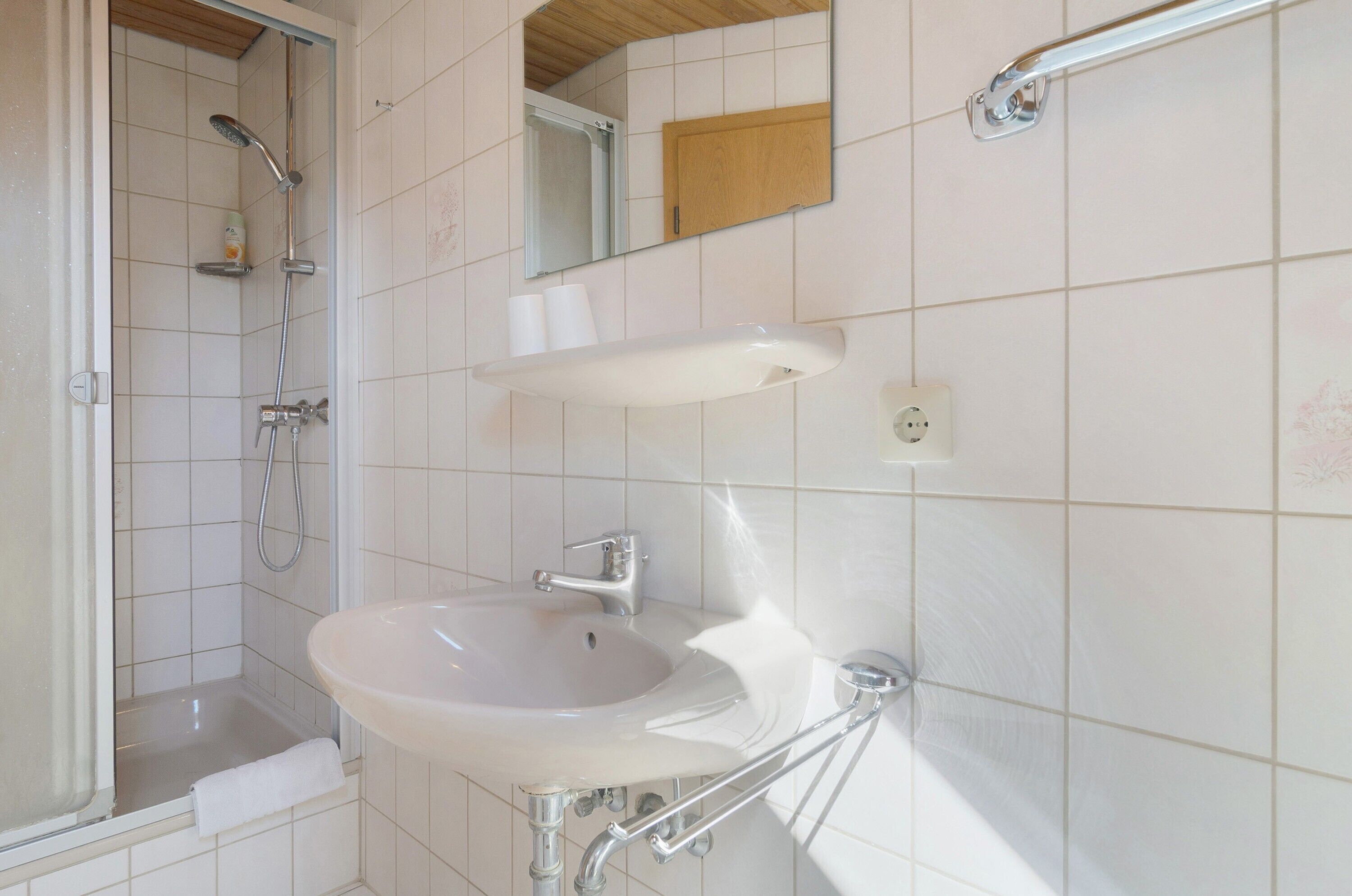 A bathroom with a shower, a sink, a mirror, and a wooden cabinet.