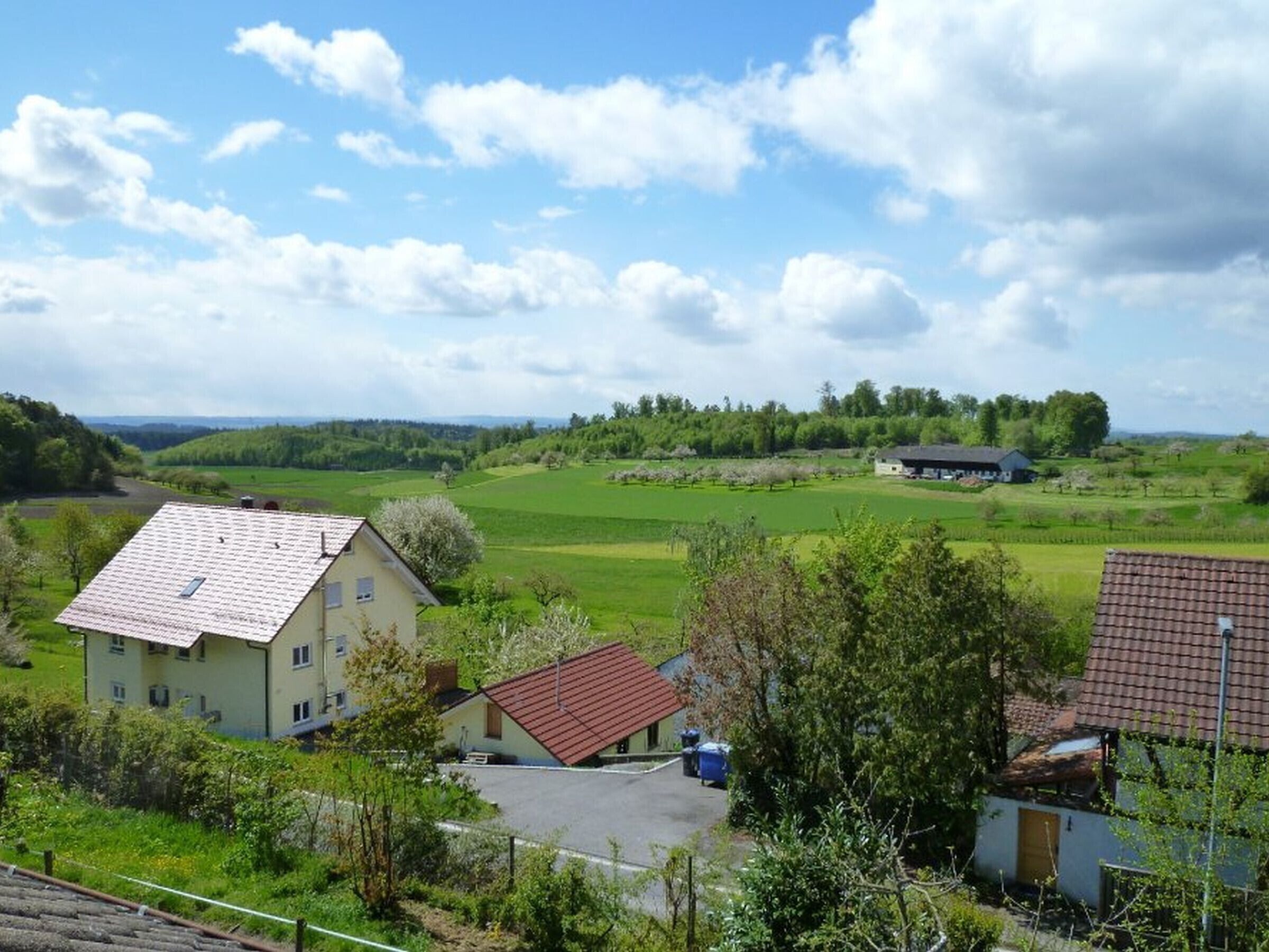 Un paisaje rural con un edificio grande, una estructura más pequeña y una zona pavimentada.