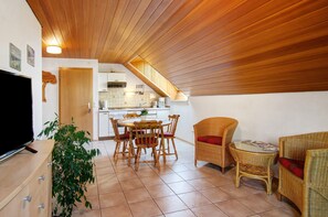 Een eetruimte met een houten plafond, een televisie, een eettafel met stoelen en een bijzettafeltje met een tijdschrift.