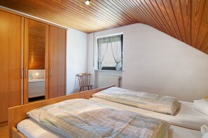 Een slaapkamer met twee bedden, een houten kledingkast, een raam met gordijnen en een radiator.