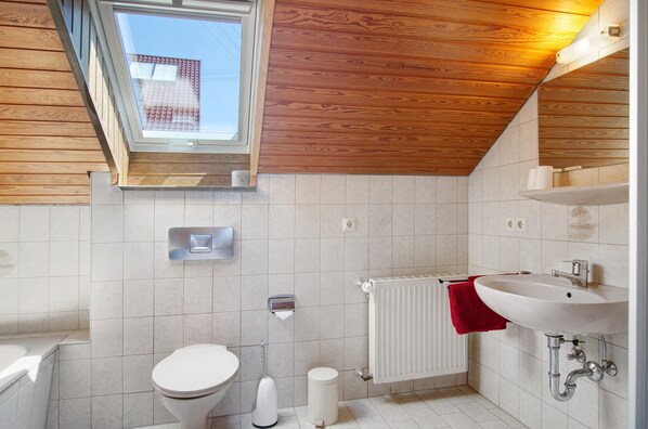 Un baño moderno con tragaluz, azulejos blancos, un inodoro, un lavabo y una toalla roja.