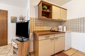 Eine kompakte Küche mit integriertem Fernseher, Holzschränken, einer Kaffeemaschine und einem Geschirrspüler.
