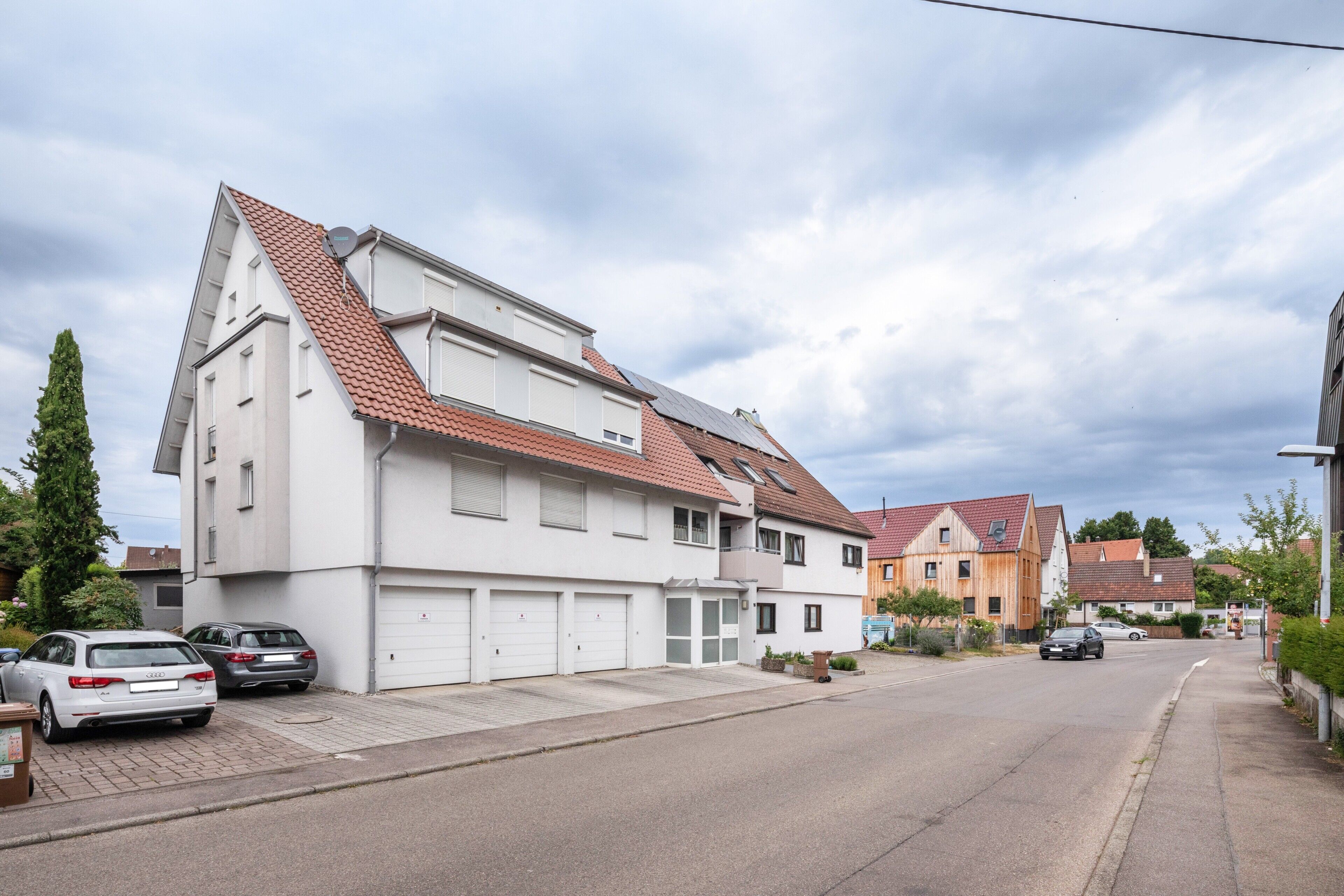 A residential street with houses, parked cars, and a clear sky.