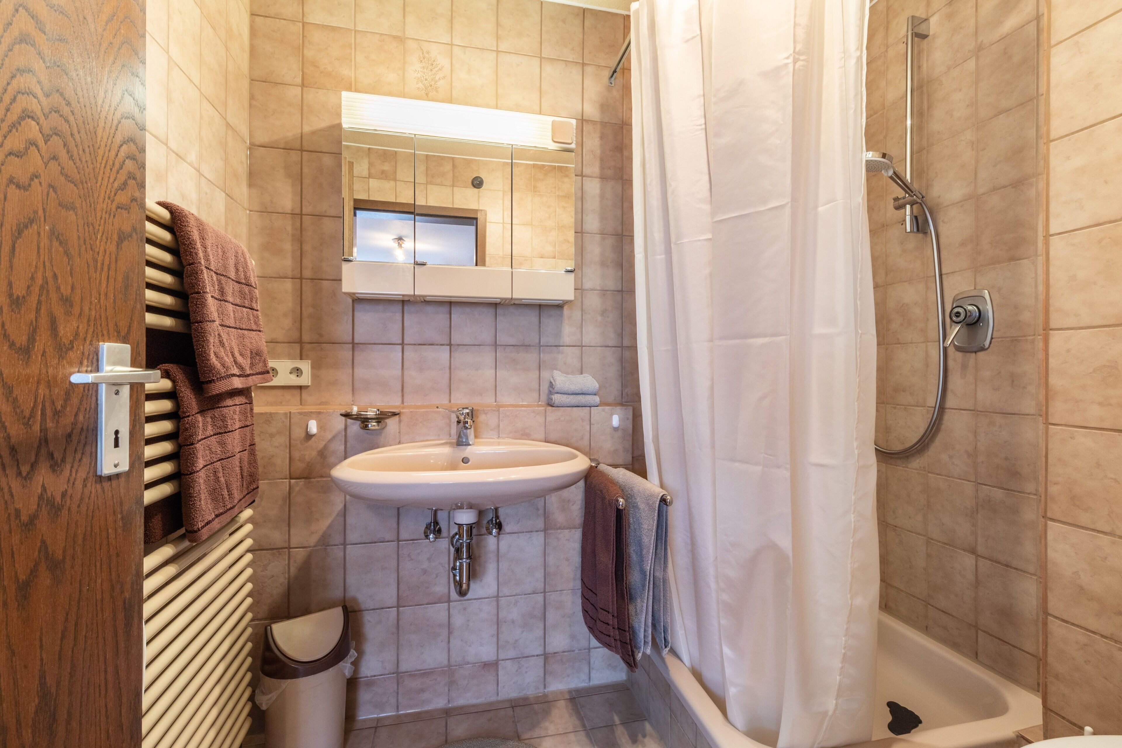 A bathroom with a sink, mirror, shower, and towel rack.
