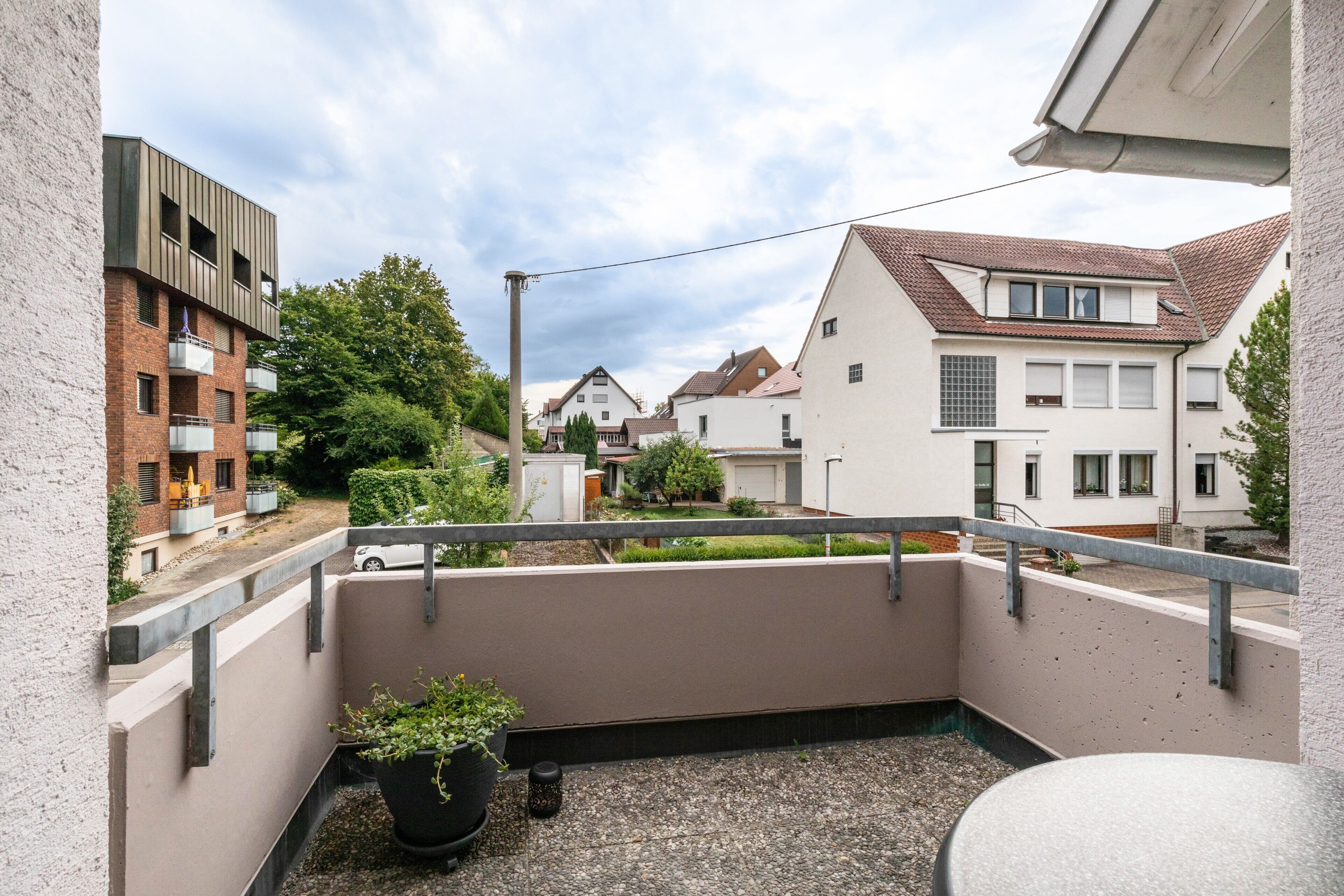 Ein Balkon mit einem Blumentopf, einer Brüstung und Blick auf benachbarte Häuser.