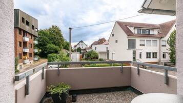 Ein Balkon mit einem Blumentopf, einer Brüstung und Blick auf benachbarte Häuser.
