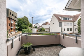 Ein Balkon mit einem Blumentopf, einer Brüstung und Blick auf benachbarte Häuser.
