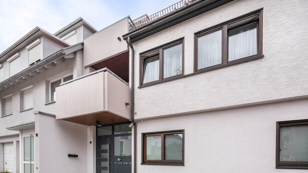 Ein modernes Wohngebäude mit flacher Fassade, großen Fenstern und einem kleinen Balkon.