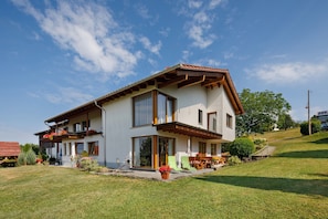 Ein zweistöckiges Haus mit Balkon, einer Terrasse und Gartenmöbeln sowie einem gepflegten Rasen.