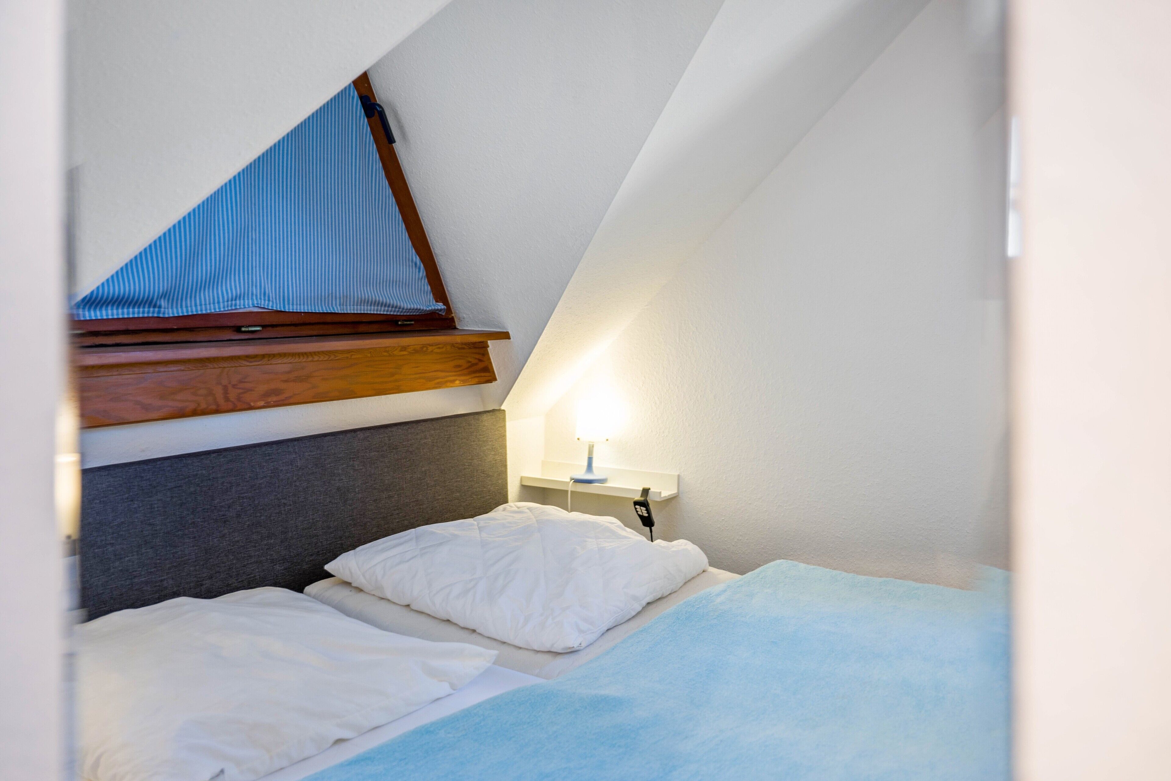 Une petite pièce triangulaire comprenant un lit, une table de chevet et une lampe.