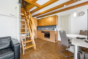 A kitchen with wooden cabinets, a built-in oven, a dining table with chairs, and a wooden staircase.