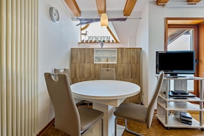 Une cuisine moderne avec une table de salle à manger ronde, deux chaises, un téléviseur posé sur un meuble et une fenêtre donnant sur un beau paysage.