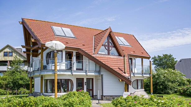 Et toetagers hus med rødt tegltag, store vinduer og en balkon.