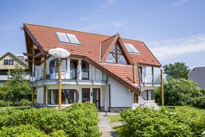 Une maison à deux étages, avec un toit recouvert de tuiles rouges, de grandes fenêtres et un balcon.