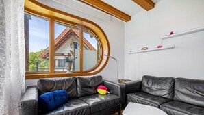 En moderne stue med en lædersofa, et lille hvidt bord og et stort vindue med udsigt til et hus.
