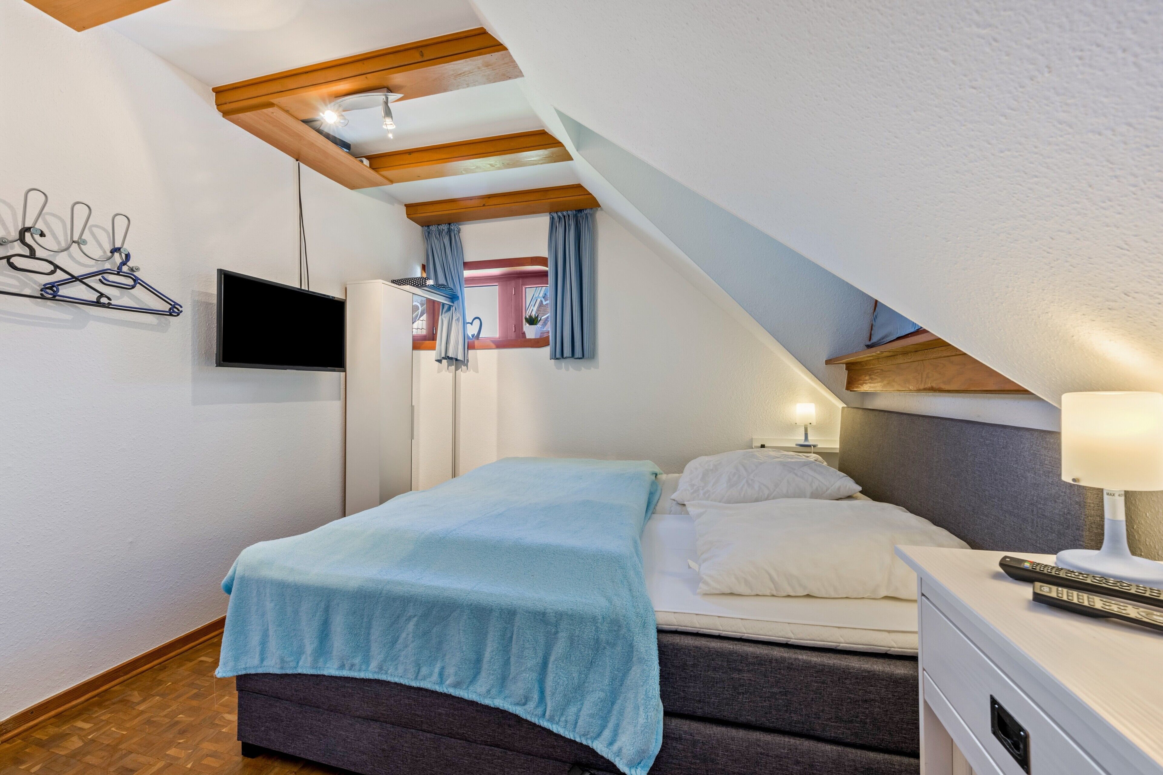 A bedroom with a bed, bedside table, lamp, and a TV mounted on the wall.