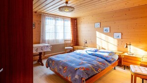 A cozy bedroom with a wooden floor, a bed with colorful bedding, a desk with a chair, and a window with sheer curtains. - Lovely apartment for 4 guests with WIFI and balcony (Lenk)