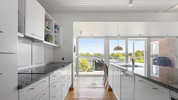 A modern kitchen with white cabinetry, a granite countertop, and a view of the outdoors through large windows.
