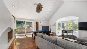 A spacious living room with a pool table, grey sofas, and a fireplace.