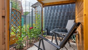 Un patio con mesa y sillas, una valla de madera y un jardín visible a través de un celosí.