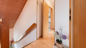 Una escalera de madera que conduce a un pasillo con una puerta de madera y un jarrón de flores.