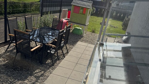 Un patio con mesa y sillas, una casita de juegos para niños y vistas a casas al fondo.