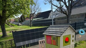 Zona de juegos infantiles con un tobogán, una casita pequeña y un patio vallado.