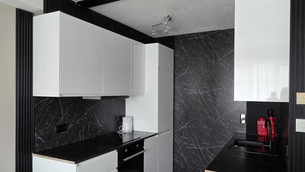 Una cocina moderna con encimeras de mármol negro, armarios blancos y una salpicadura trasera negra.