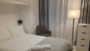 Una habitación de hotel ordenada con una cama grande, una mesita de noche, una silla y una lámpara.