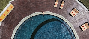Ein kreisförmiger Pool mit umlaufender Liegefläche, Liegestühlen und einer kleinen Sitzecke.