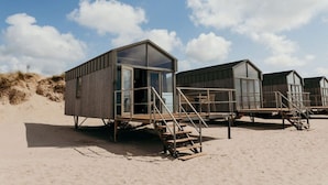 Een houten constructie aan het strand, met glazen ingang en een trap naar een terras.
