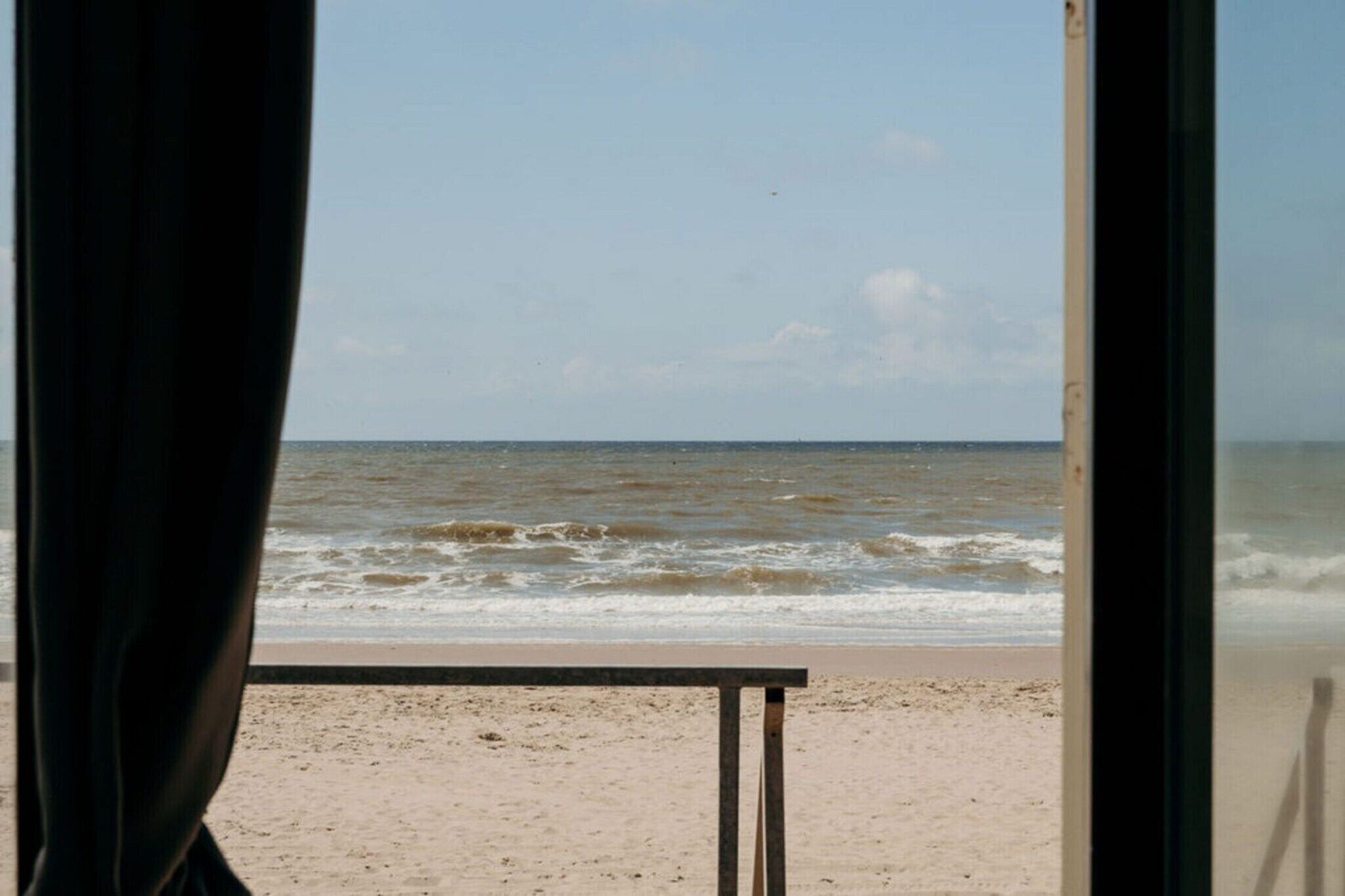 Vista a la playa a través de una ventana, con una mesa en primer plano.