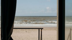 Uitzicht op het strand door een raam, met een tafel op de voorgrond.