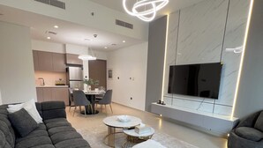 Un salon moderne avec un canapé d’angle, un coin repas et une cuisine en arrière-plan.