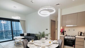 Une cuisine moderne dotée d’un four encastré, un coin repas avec une table ronde et des chaises, et un salon avec un canapé et une grande fenêtre.