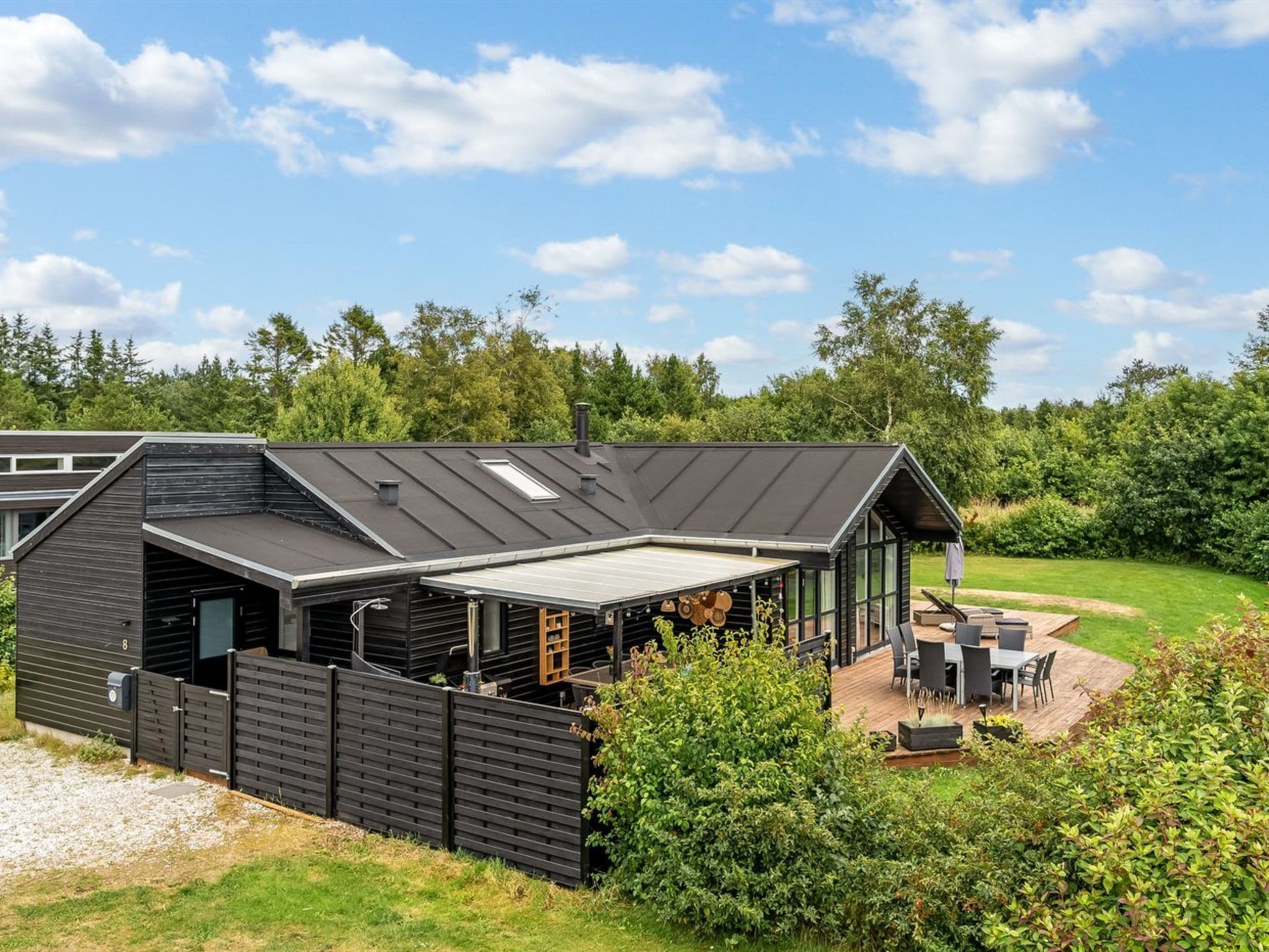 Een modern huis met een overdekte patio, een omheinde tuin en uitzicht op het omliggende groen.