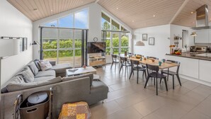 A spacious living area with a large sofa, dining table, and chairs, connected to a kitchen and a balcony with large windows. - "Smilla" - 1.1km from the sea by Interhome (Hals)