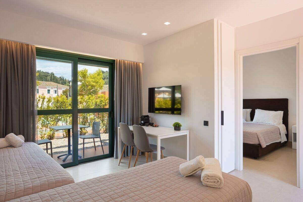 A hotel room with two beds, a desk, a TV, and a balcony with outdoor seating.
