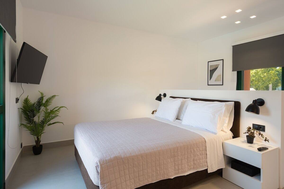 A modern bedroom with a bed, bedside tables, a wall-mounted TV, and a potted plant.
