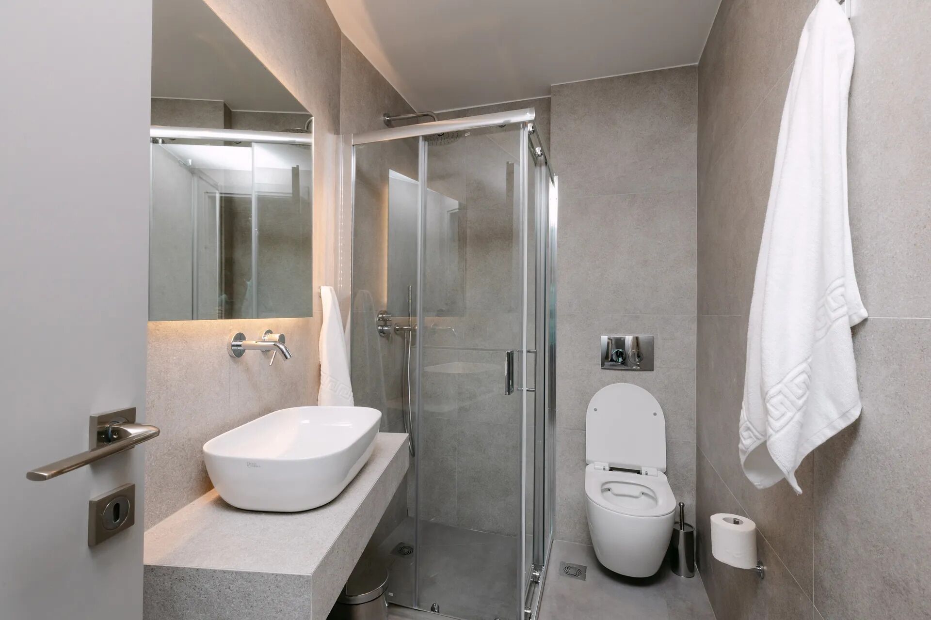 Uma casa de banho moderna com chuveiro envolto em vidro, lavatório branco e sanita.