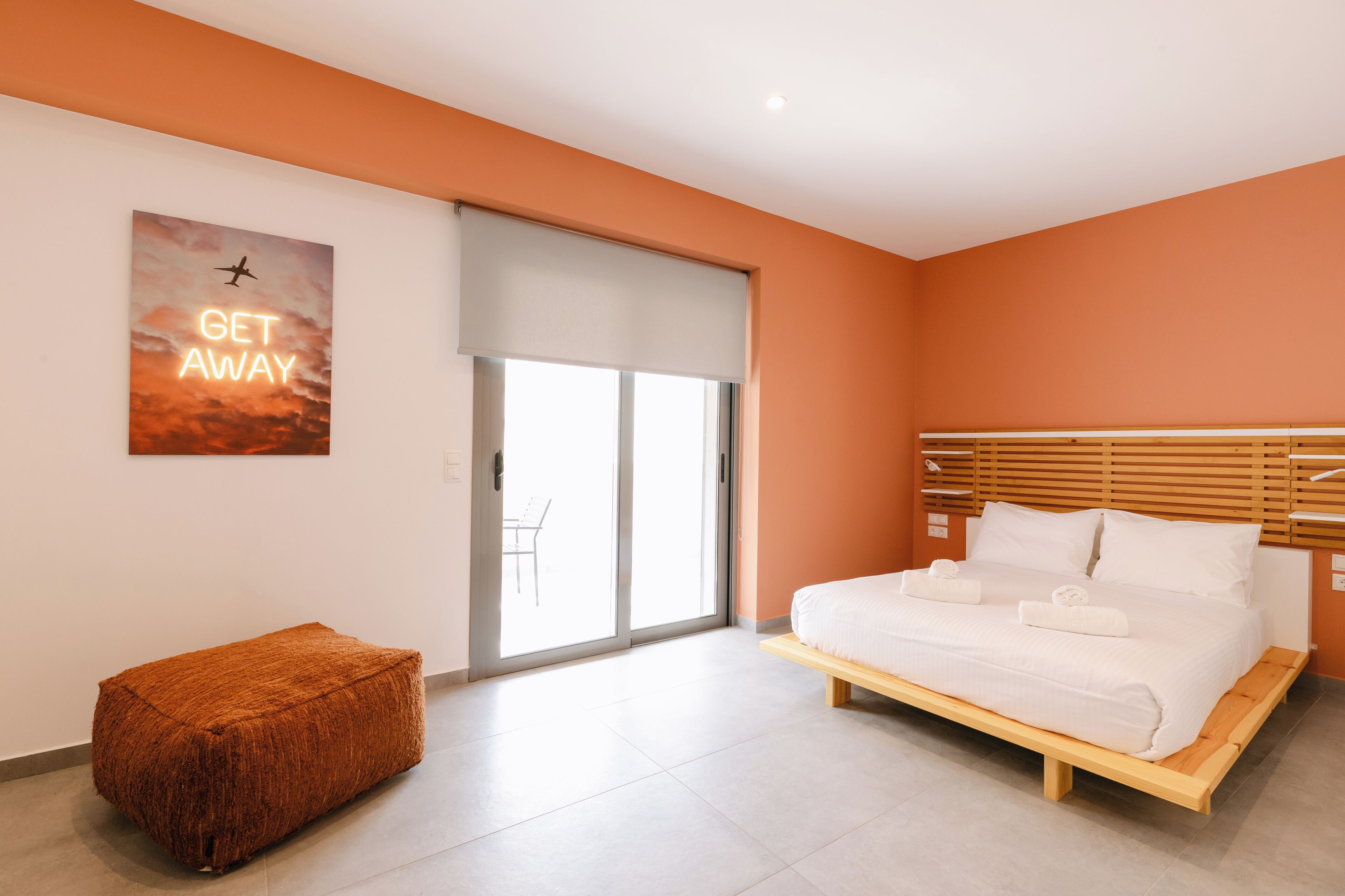 Quarto moderno com cama, um banquinho e porta deslizante.