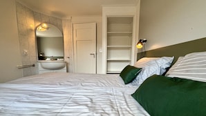 A bedroom with a bed, green pillows, a bedside lamp, a mirror, and a bathroom with a sink.