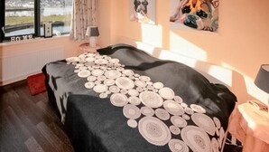 Une chambre avec un grand lit, une fenêtre donnant sur un plan d’eau et deux tableaux accrochés au mur.