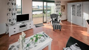 Un salon comprenant un téléviseur, un canapé, un fauteuil à rayures et une table basse ornée de motifs floraux.