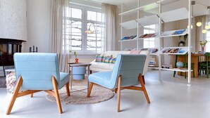 A modern living room with two light blue armchairs, a white sofa, and a white bookshelf filled with books and decorative items.