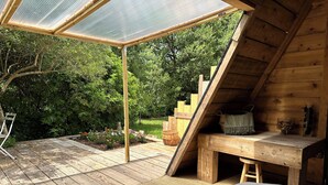 Een houten terras met een pergola, een houten bank en een rustieke tafel.