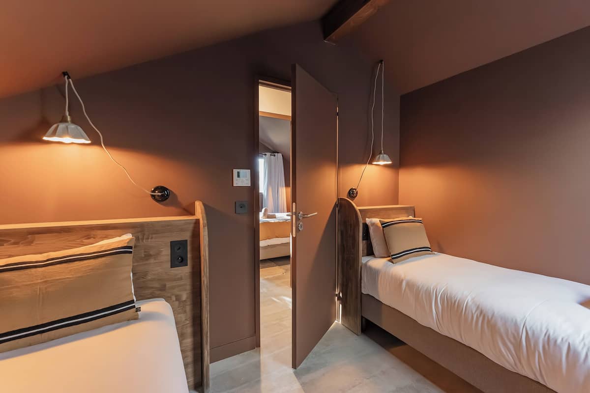 A bedroom with two beds, a wooden headboard, bedside lamps, and a door leading to another room.