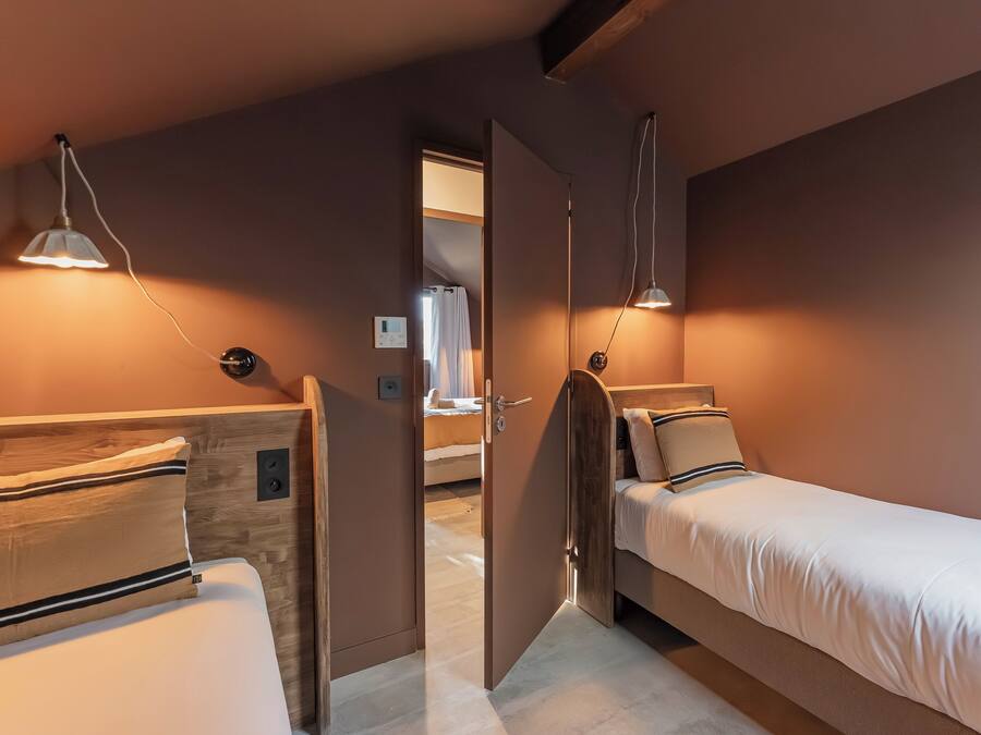 Un dormitorio con dos camas, cabeceros de madera, lámparas de noche y una puerta que da a otra habitación.