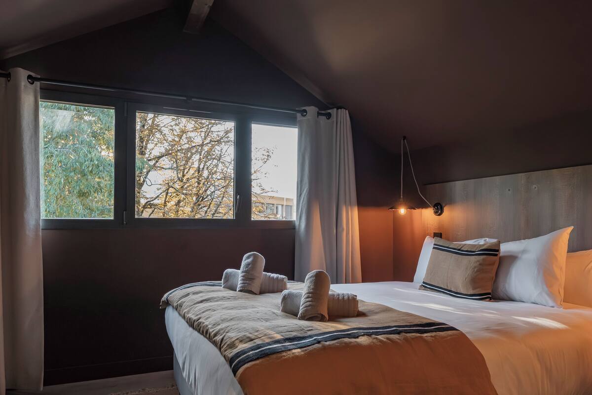 A hotel room with a large bed, a window with curtains, and a wall-mounted light fixture.